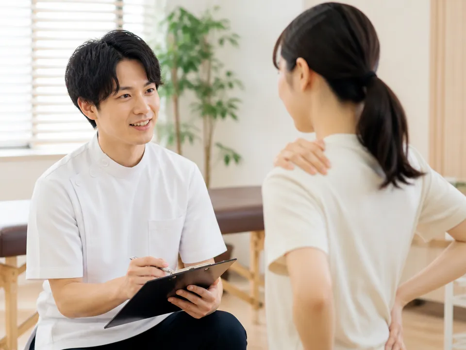 肩こりや腰痛の悩みを相談する患者と接骨院スタッフ