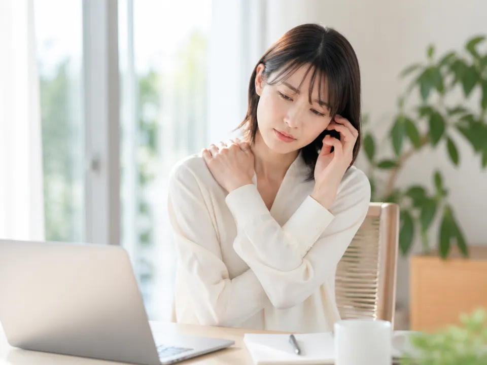 肩こりと頭痛に悩みながら耳と肩を触っている人