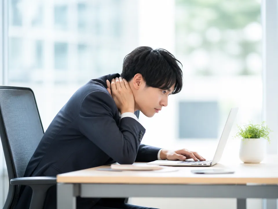デスクワーク中に頭が前に出た姿勢で首や肩に負担がかかっている様子