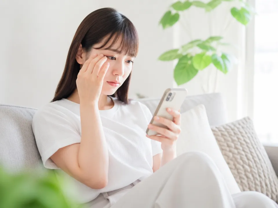 まぶたのマッサージ方法をスマホで調べて不安そうな女性