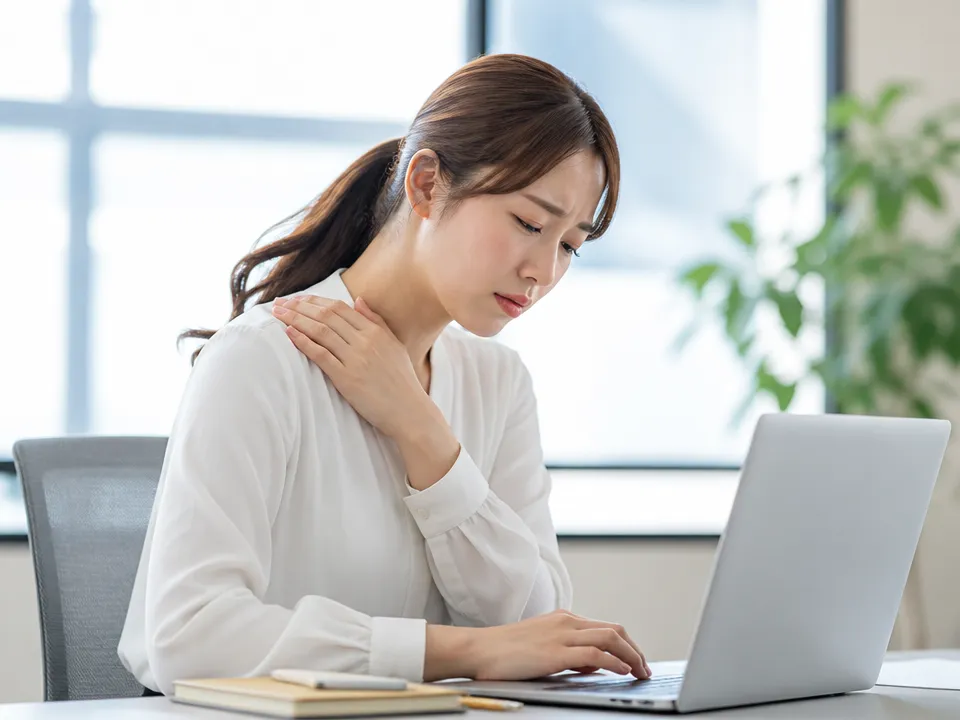 デスクワーク中に前かがみ姿勢で胸と肩がつらい女性