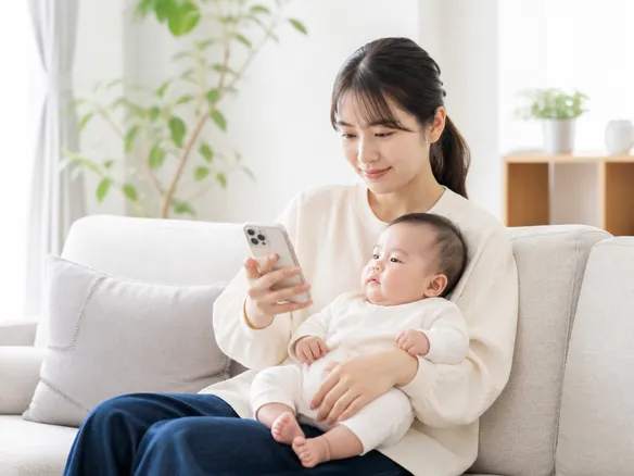 赤ちゃんを抱えながら産後の骨盤や腰痛について相談先を探す母親のイメージ