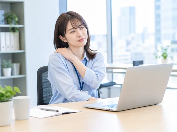 デスクワークで慢性的な肩こりに悩む人の様子