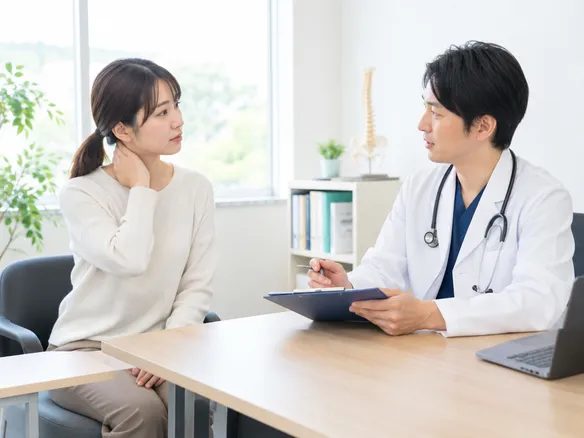 首の付け根のこりについてセルフケア継続か受診かを相談している場面