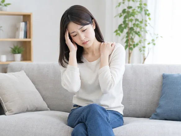 肩こりと頭痛吐き気が続き不安そうに座る人