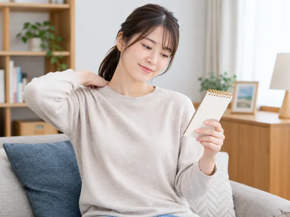 産後肩こりのセルフチェックをメモしながら肩を回す女性