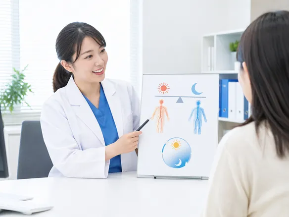 交感神経と副交感神経のバランスと眠気の関係を説明する図を指さす人
